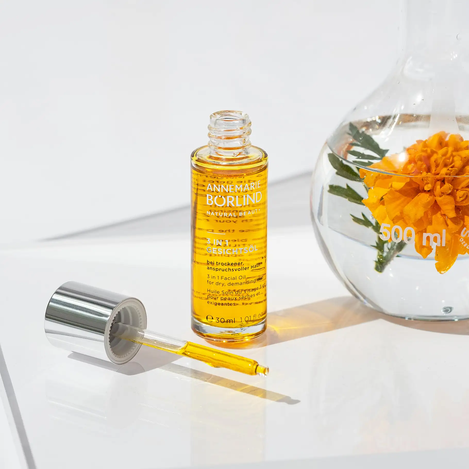 ANNEMARIE BÖRLIND 3 in 1 Gesichtsöl in Glasflasche mit Pipette und orangefarbener Blume im Glasgefäß