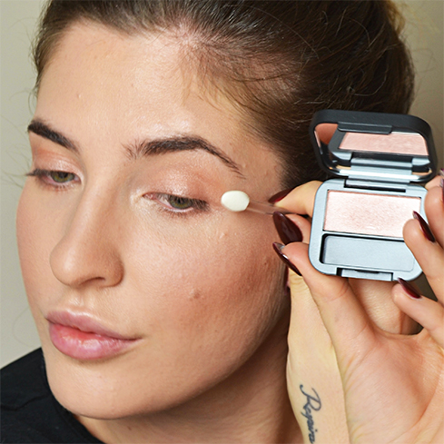 Frau trägt schimmernden roséfarbenen Lidschatten mit Applikator auf das Augenlid auf, Nahaufnahme