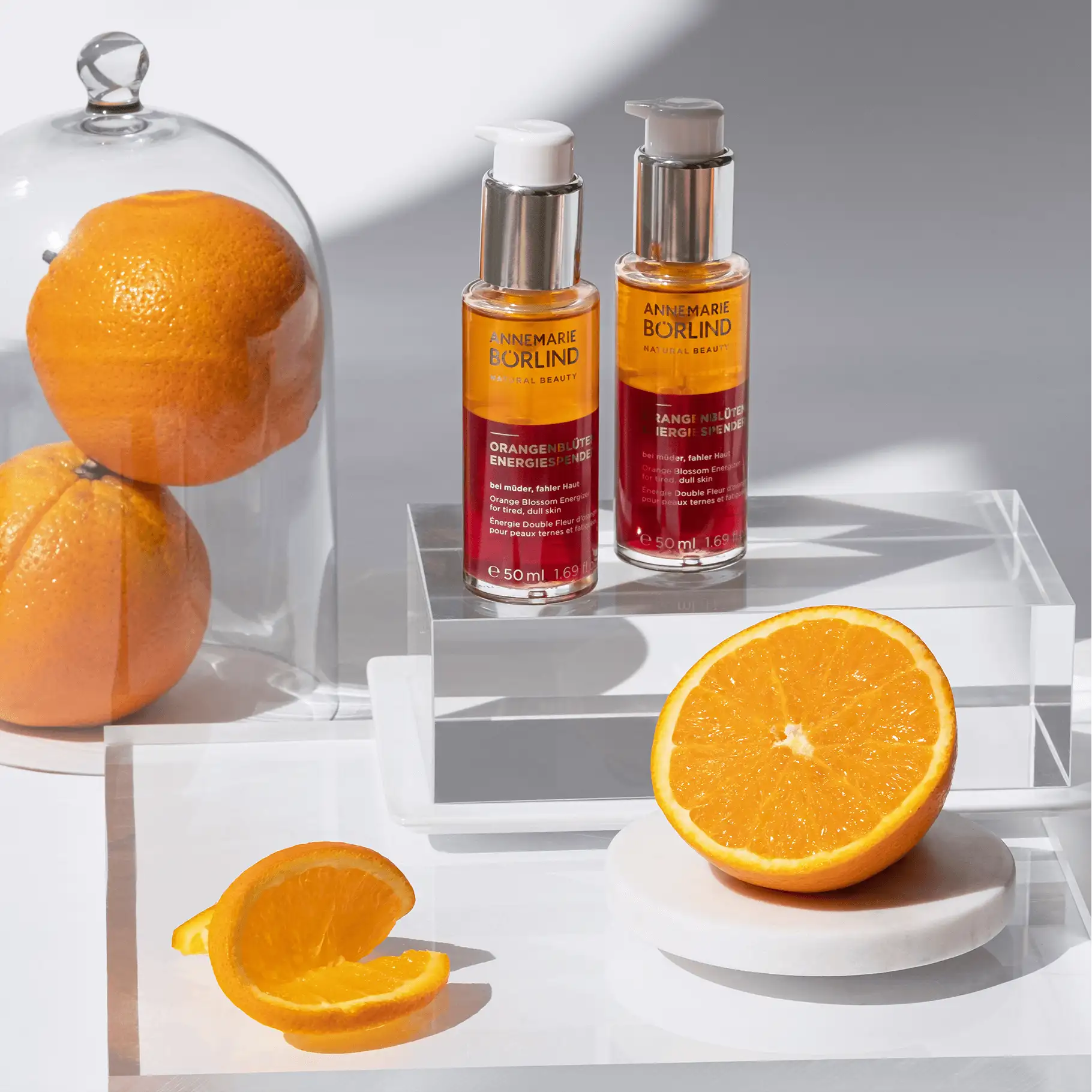 ANNEMARIE BÖRLIND Orangenblüten Energiespender Serum mit frischen Orangen und Glasglocke auf weißem Hintergrund