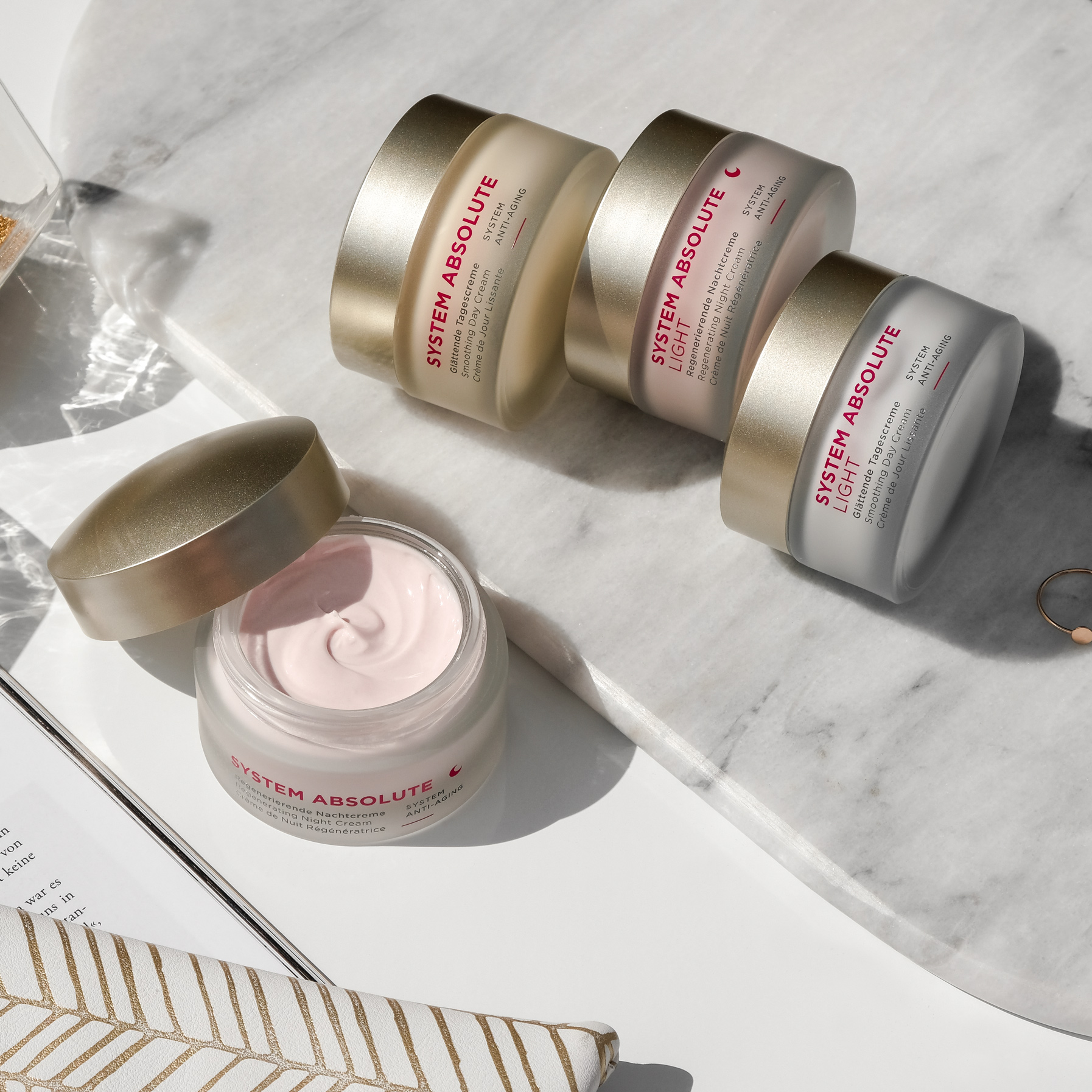 SYSTEM ABSOLUTE Gesichtscremes in Glasdosen, eine geöffnet mit rosafarbener Creme, auf Marmoruntergrund