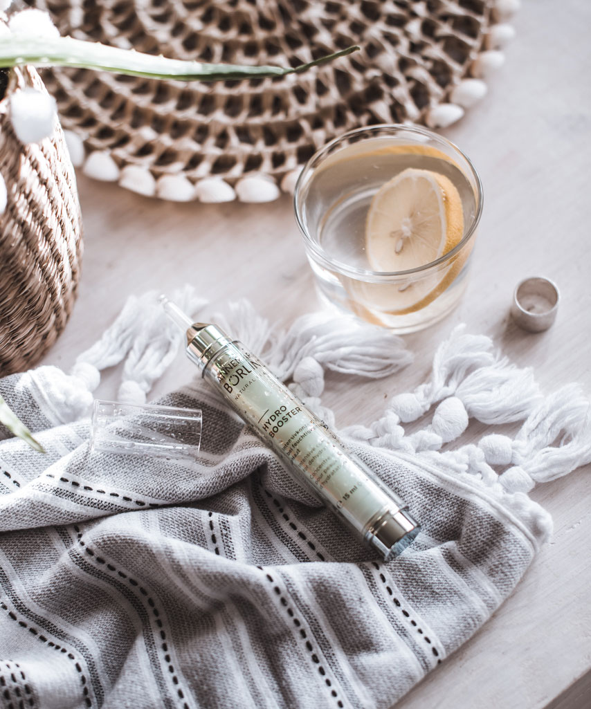 ANNEMARIE BÖRLIND Hydro Booster Serum auf grauem Stofftuch neben Glas mit Zitronenscheibe und Korb