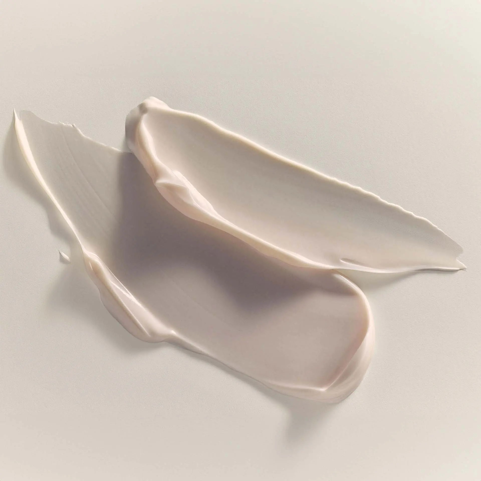 Zarte, cremige Textur einer hellbeigen Nachtcreme auf hellem Untergrund