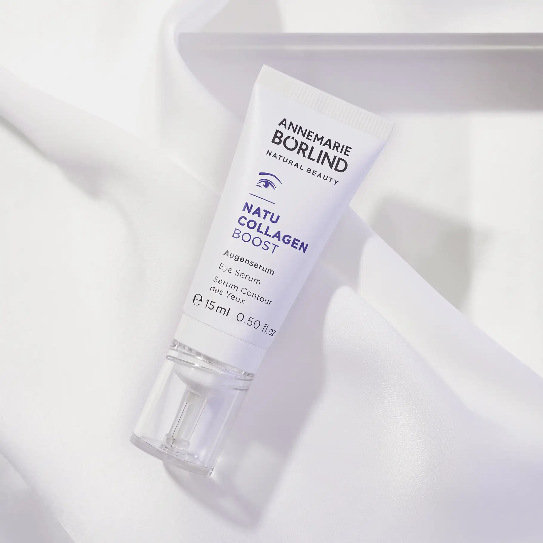 ANNEMARIE BÖRLIND NATU COLLAGEN BOOST Augenserum in weißer Tube mit transparentem Pumpspender auf weißem Stoff