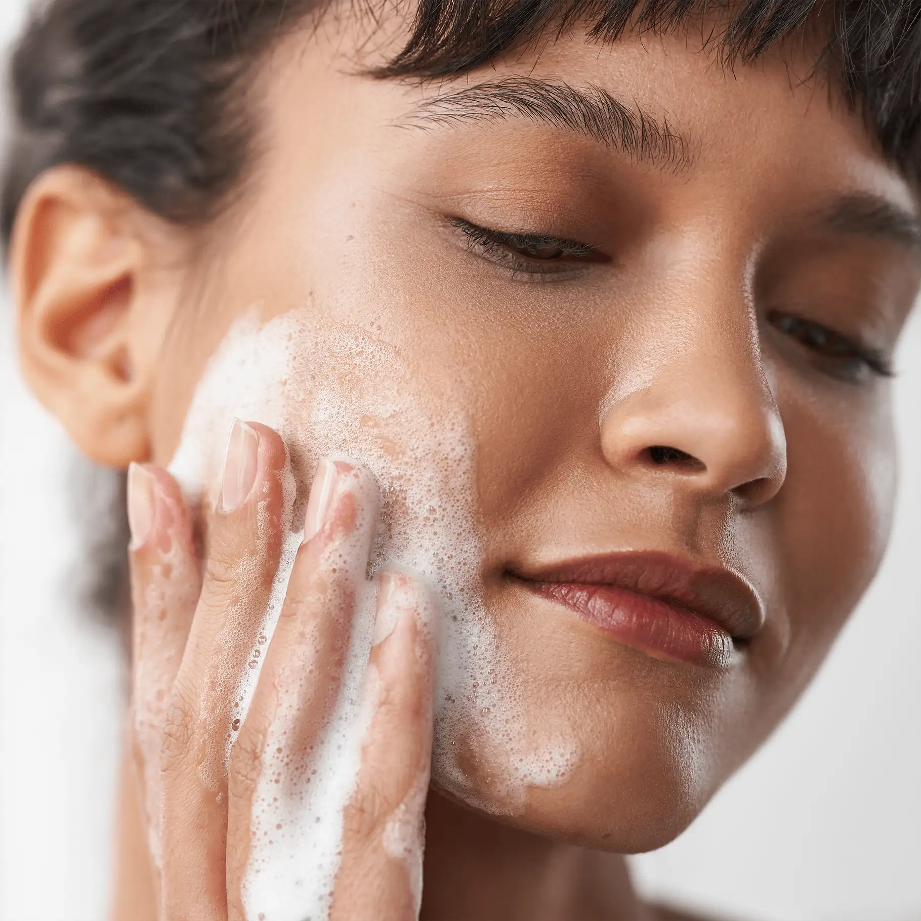 Frau reinigt Gesicht mit schaumigem Mousse, Nahaufnahme der Gesichtshaut und Hand berührt Wange