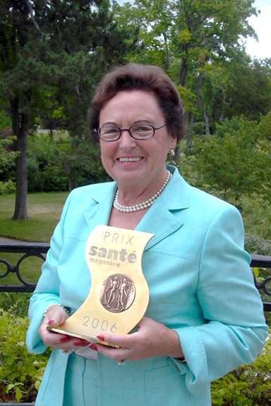 Annemarie Lindner in hellblauem Kostüm hält PRIX santé magazine Trophäe von 2006 in einem Park