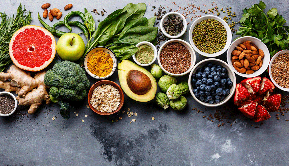 Verschiedene Superfoods wie Grapefruit, Avocado, Heidelbeeren, Mandeln, Brokkoli, Spinat, Haferflocken und Gewürze auf gra...