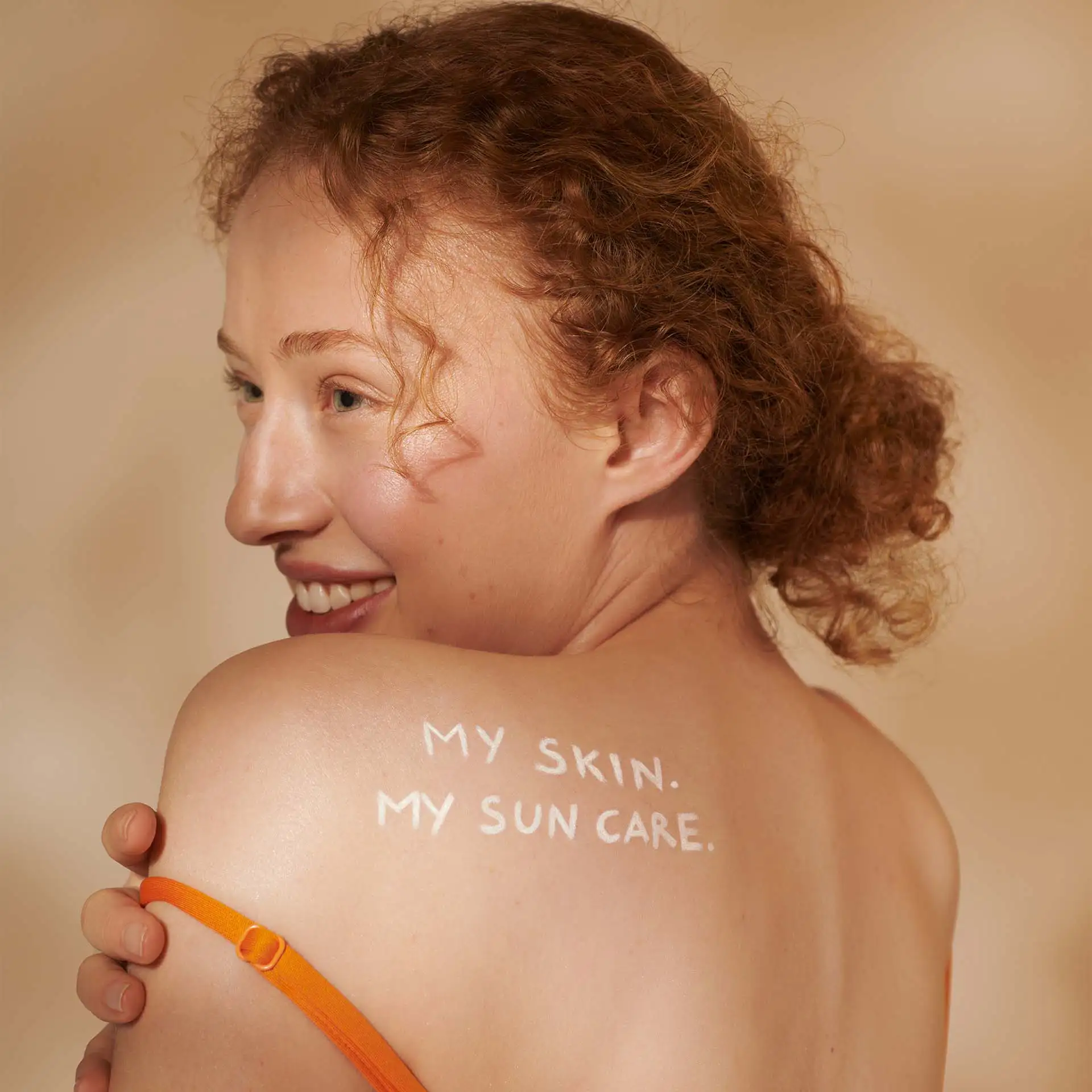 Frau mit roten Locken lächelt, Schriftzug „MY SKIN. MY SUN CARE.“ auf nackter Schulter sichtbar