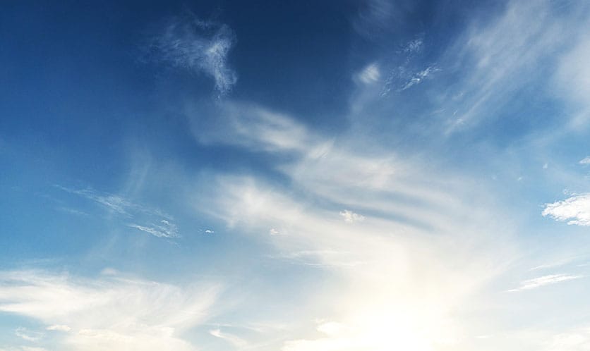 Blauer Himmel mit weißen, dünnen Wolken und strahlender Sonne am unteren Bildrand
