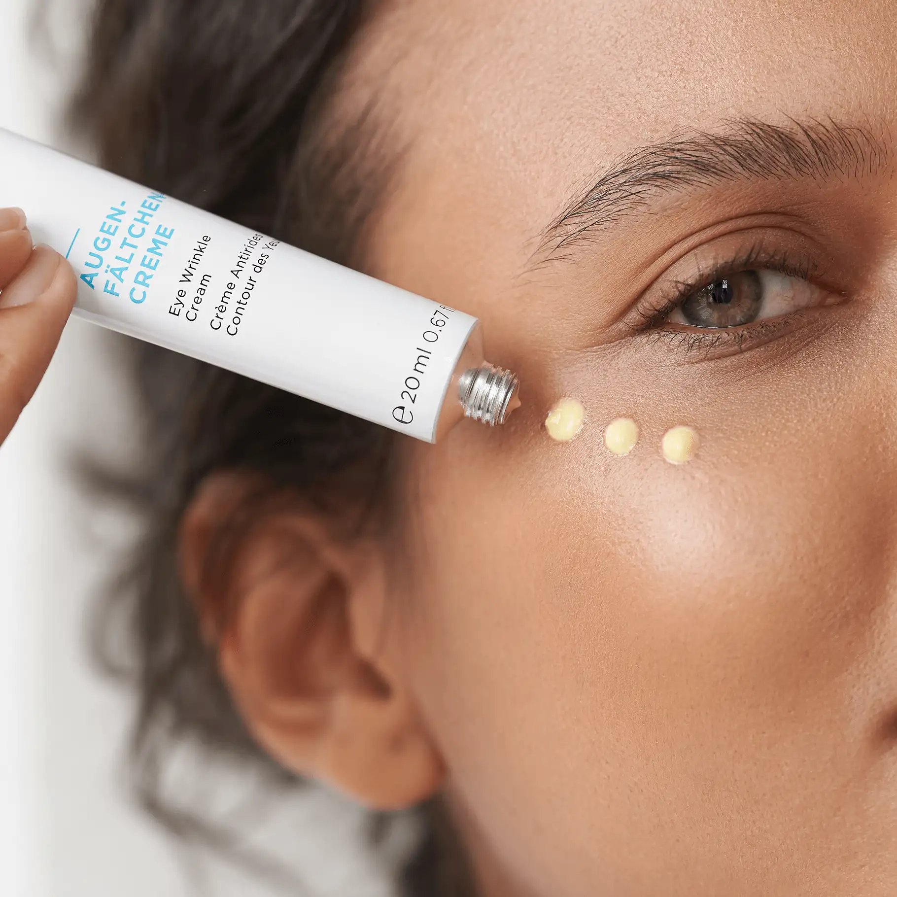 Auftragen von AUGEN-FÄLTCHEN-CREME in drei Punkten unter das Auge auf helle Haut
