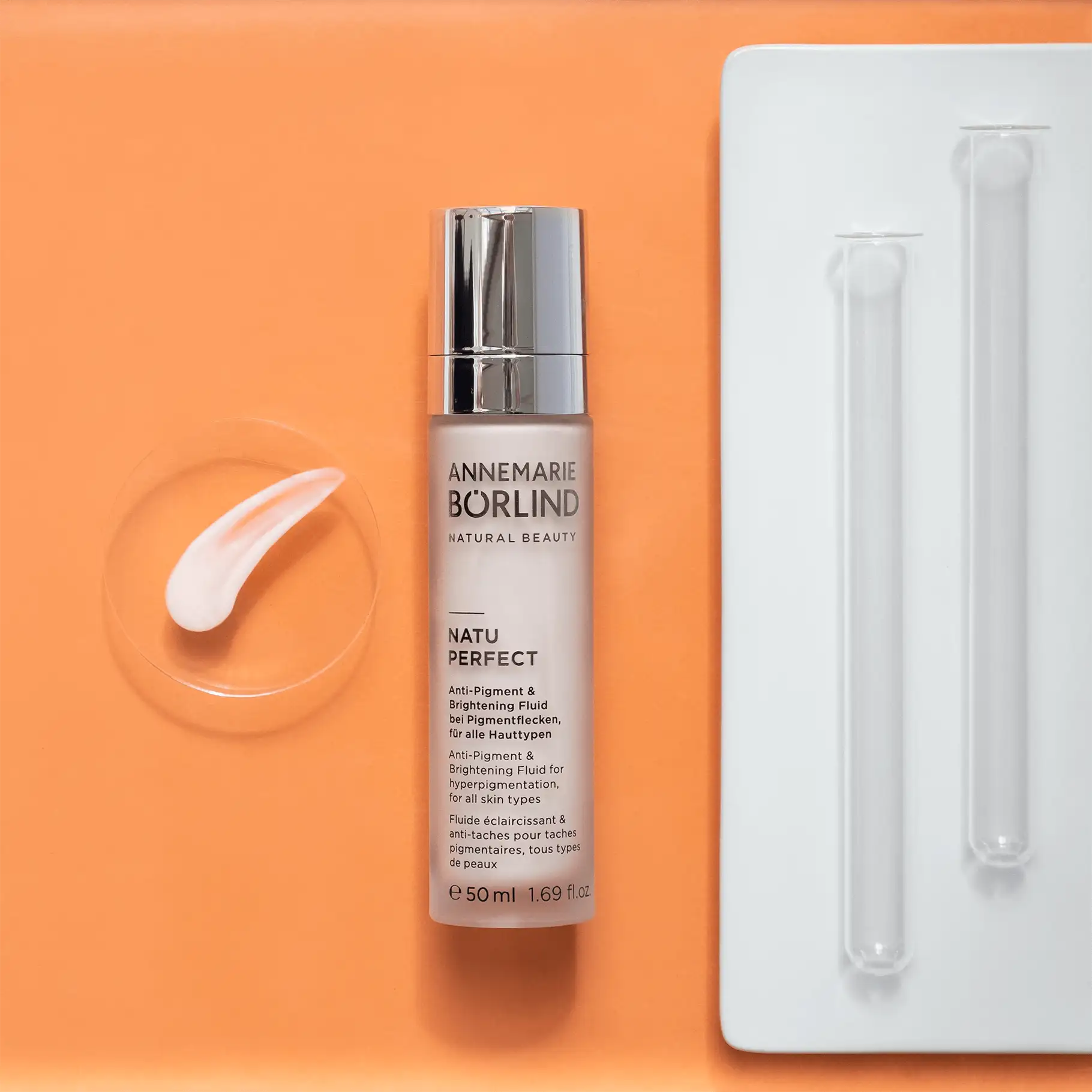 ANNEMARIE BÖRLIND NATU PERFECT Anti-Pigment & Brightening Fluid 50 ml mit Cremeprobe und Reagenzgläsern auf orangefarbenem...