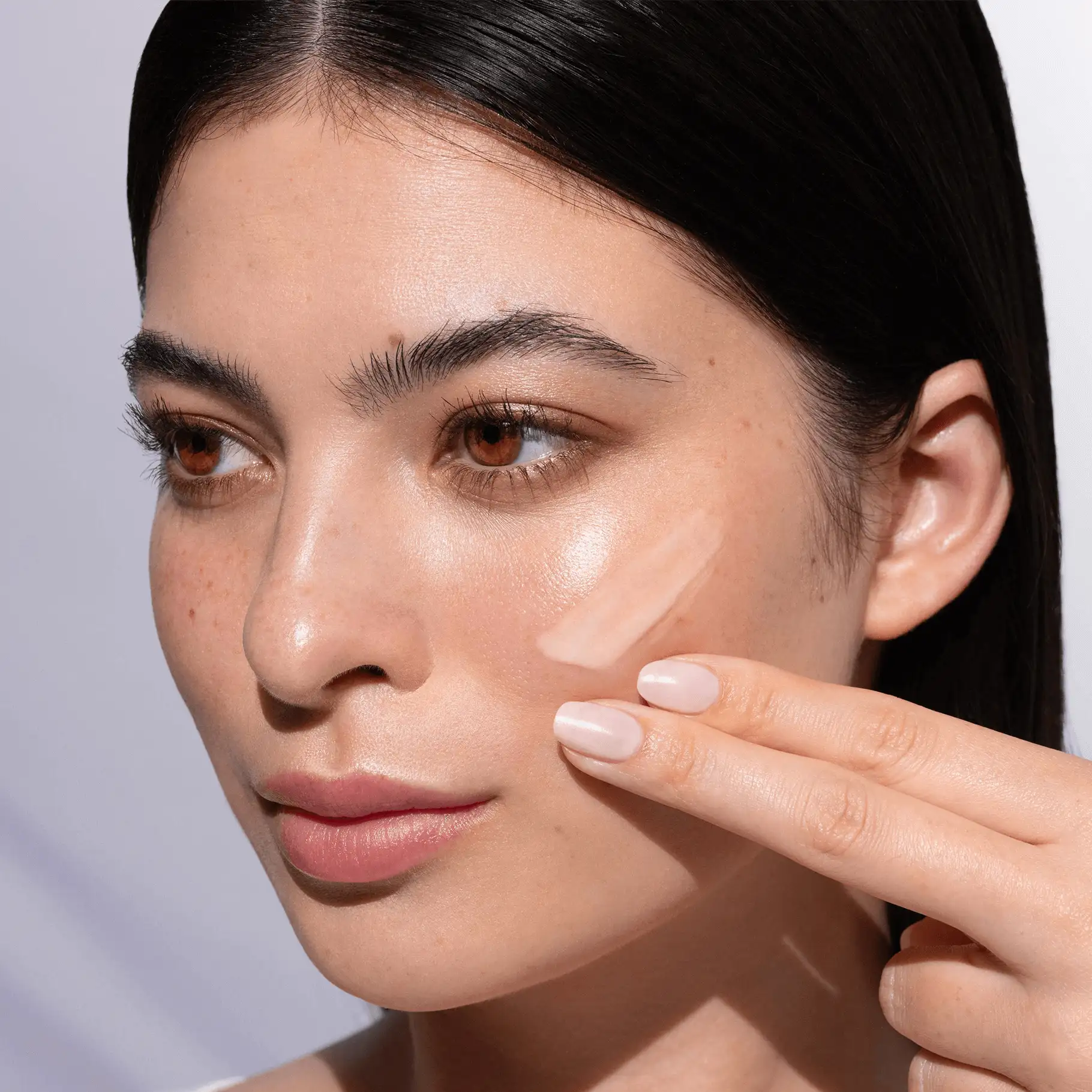 Frau trägt NATUCOLLAGEN Gesichtsfluid auf Wange auf, Nahaufnahme mit natürlichem Licht und gepflegter Haut