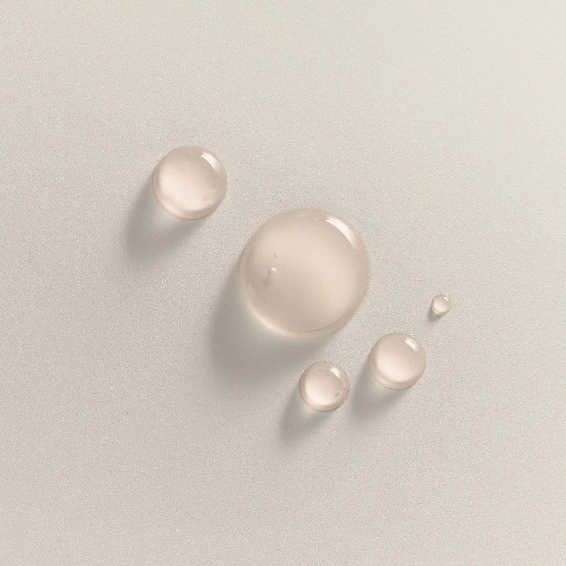 Transparente, flüssige Tropfen unterschiedlicher Größe auf hellem, mattem Untergrund