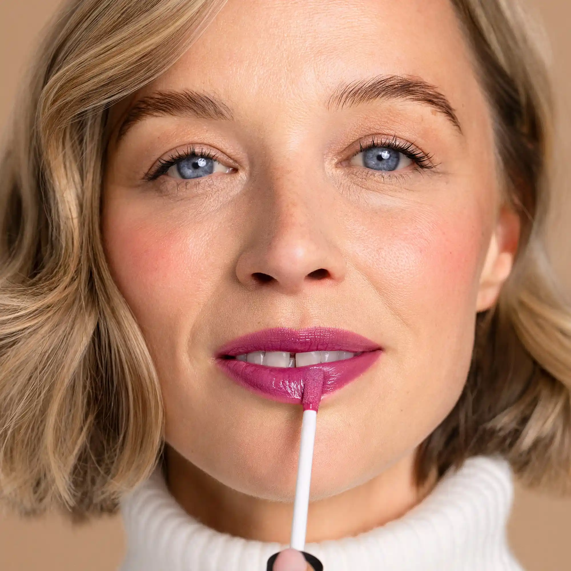 Frau trägt ANNEMARIE BÖRLIND NATURAL VOLUME LIP GLOSS in Farbe Snuggle Berry auf, Nahaufnahme mit natürlichem Make-up und beigem Hintergrund