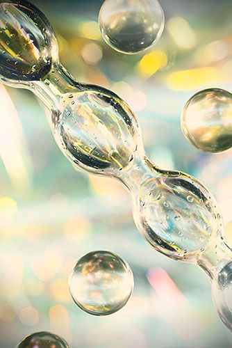 Transparente, glänzende Kapseln und Kugeln mit Lichtreflexen vor unscharfem, pastellfarbenem Hintergrund