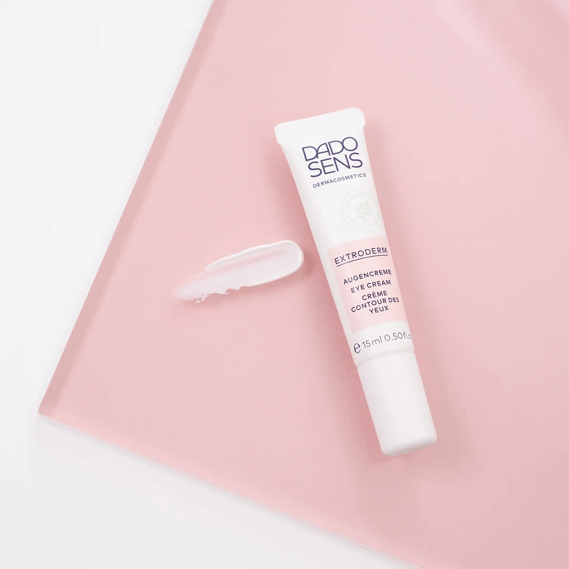 DADO SENS EXTRODERM Augencreme 15 ml Tube mit Cremeprobe auf rosa Untergrund
