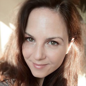Nahaufnahme einer lächelnden Frau mit braunen Haaren und natürlichem Licht auf der linken Gesichtshälfte