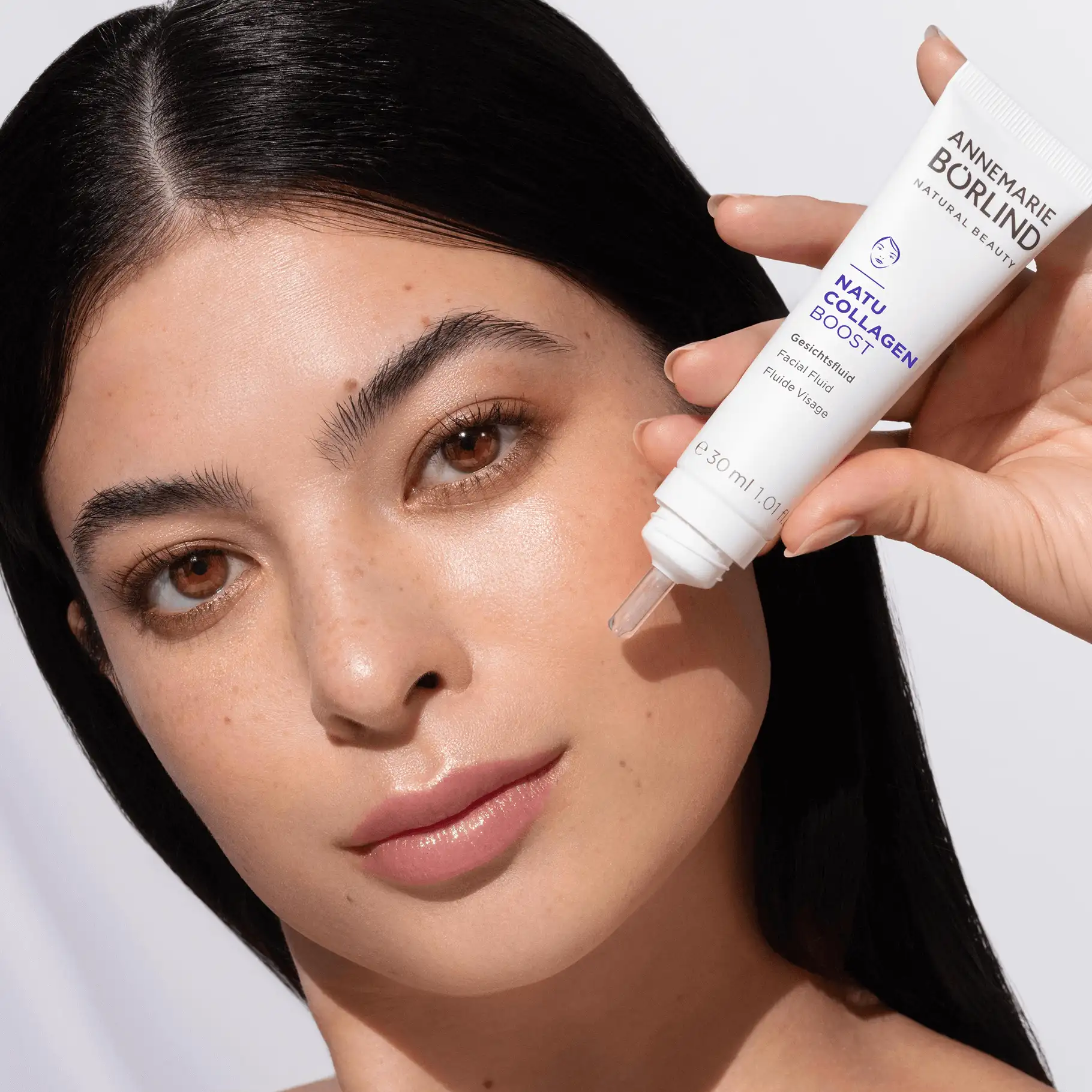 Frau trägt ANNEMARIE BÖRLIND NATU COLLAGEN BOOST Gesichtsfluid auf die Wange auf
