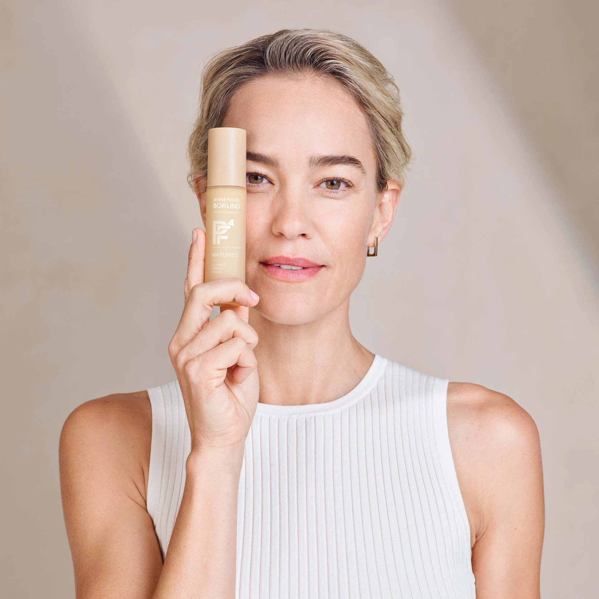 Frau hält ANNEMARIE BÖRLIND NATUNEO Ultimate Firming Serum nah am Gesicht, neutraler Hintergrund