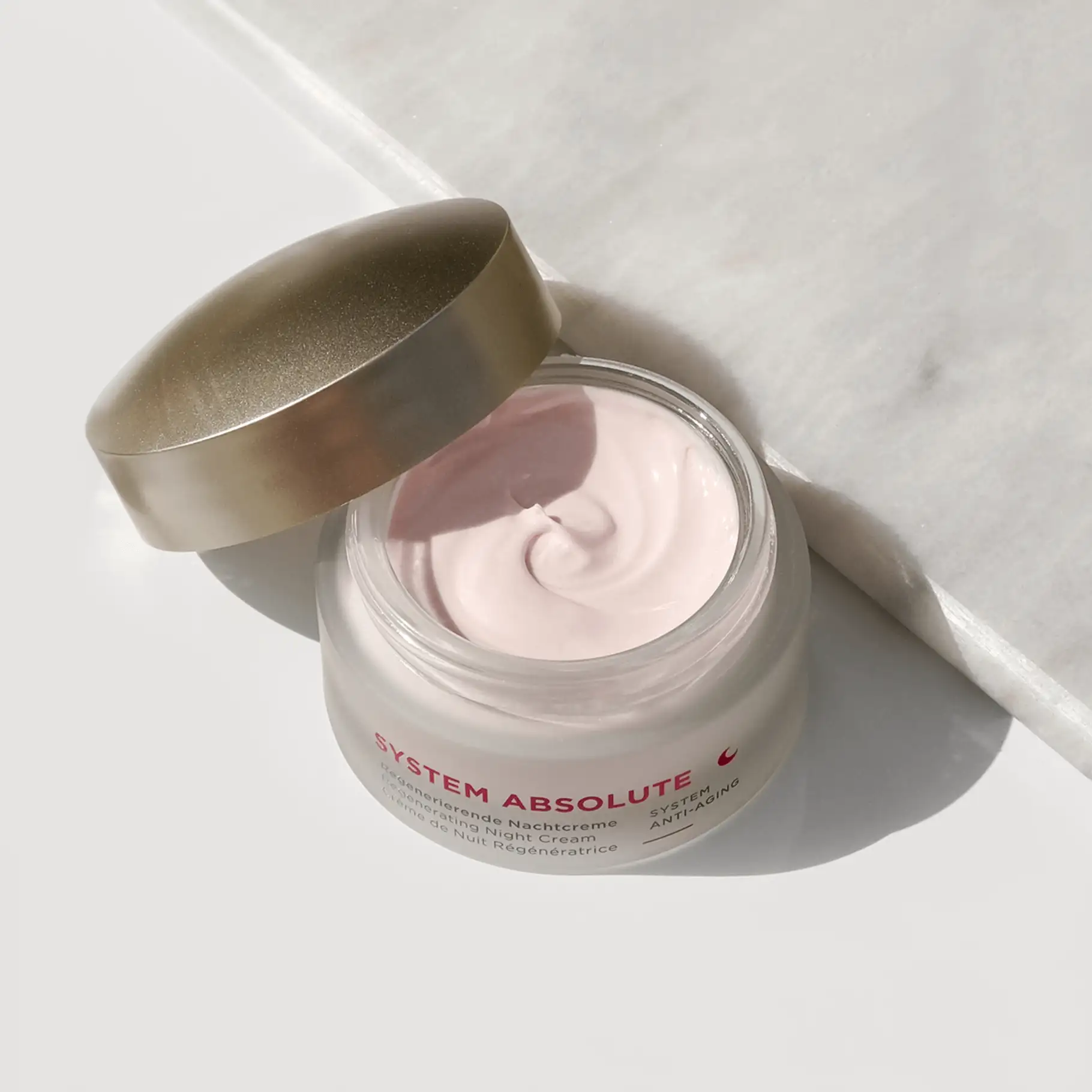 SYSTEM ABSOLUTE regenerierende Nachtcreme im geöffneten Tiegel mit cremiger, rosafarbener Textur auf hellem Untergrund