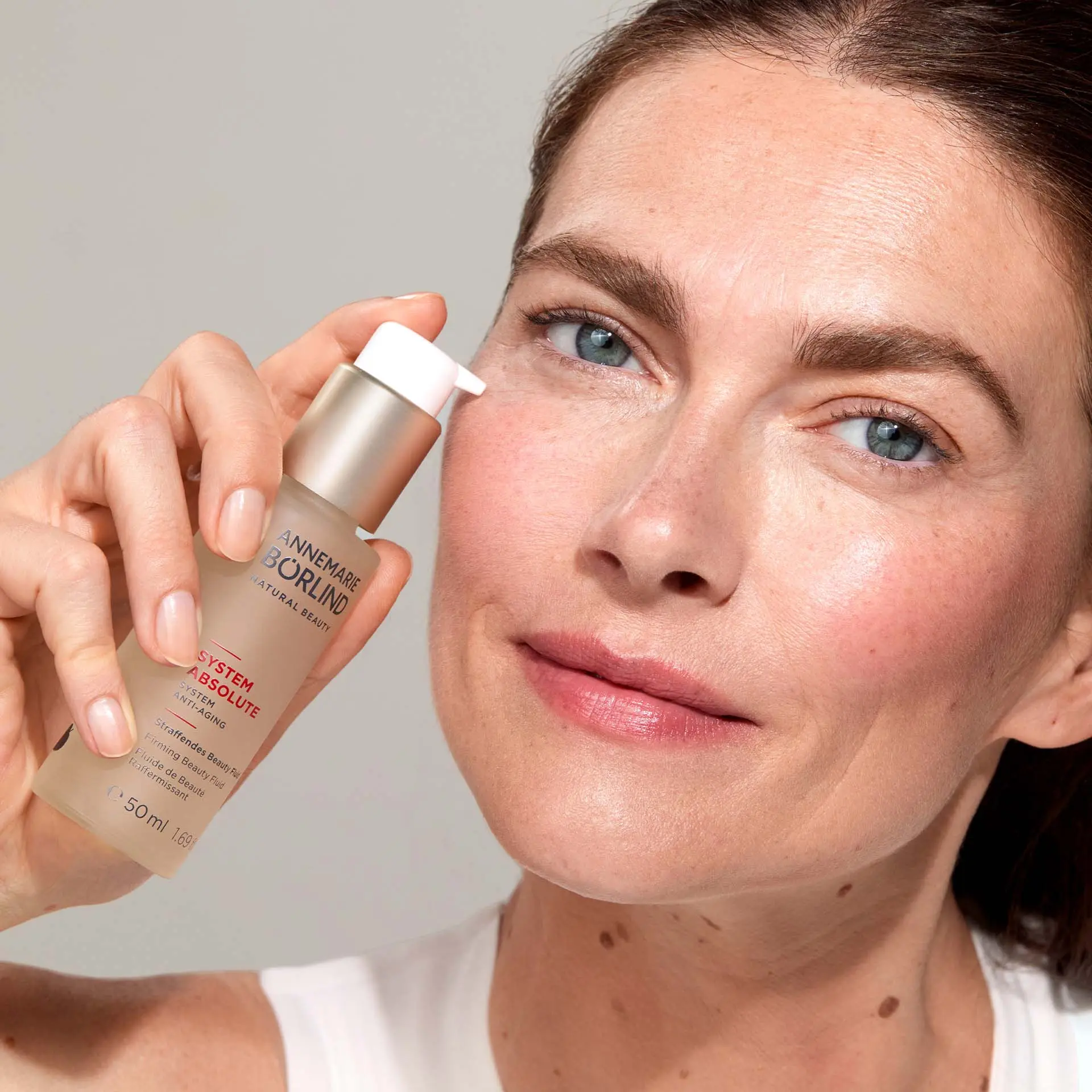 Frau hält SYSTEM ABSOLUTE Straffendes Beauty Fluid vor Gesicht