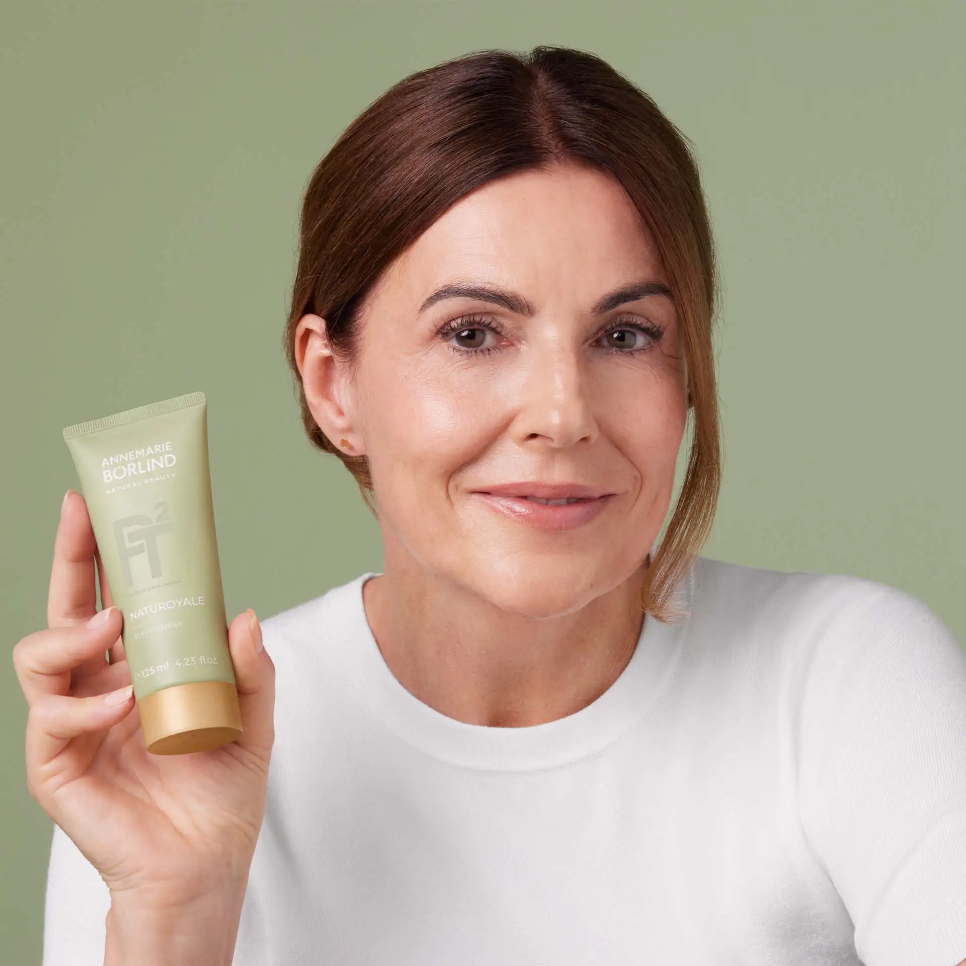 Frau hält ANNEMARIE BÖRLIND NATUROYALE Skin Cleanser in Hand vor grünem Hintergrund