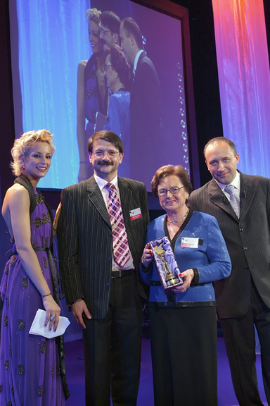 Vier Personen in festlicher Kleidung bei einer Preisverleihung, eine Frau hält eine Auszeichnung in der Hand