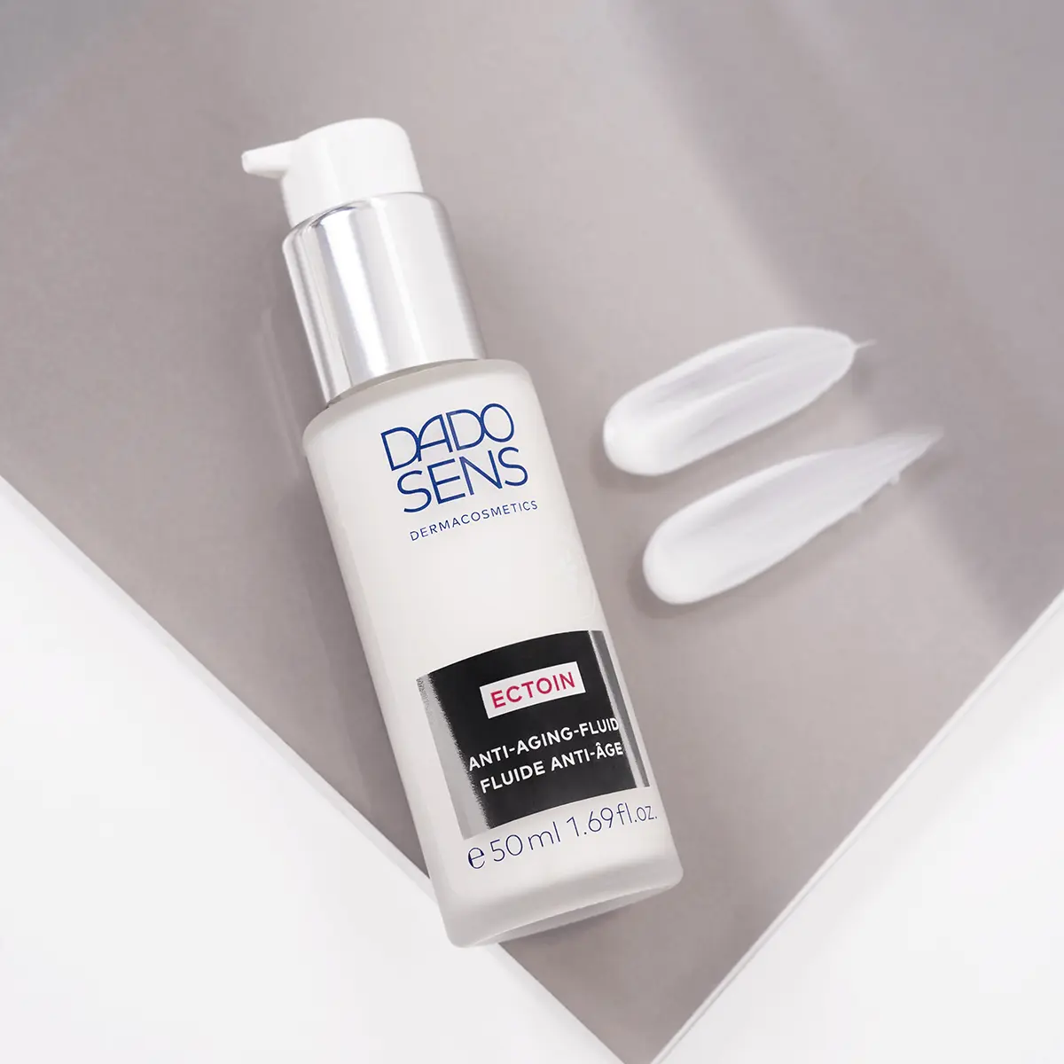 DADO SENS ECTOIN Anti-Aging-Fluid 50 ml mit Pumpspender und zwei Cremetexturproben auf grauem Untergrund
