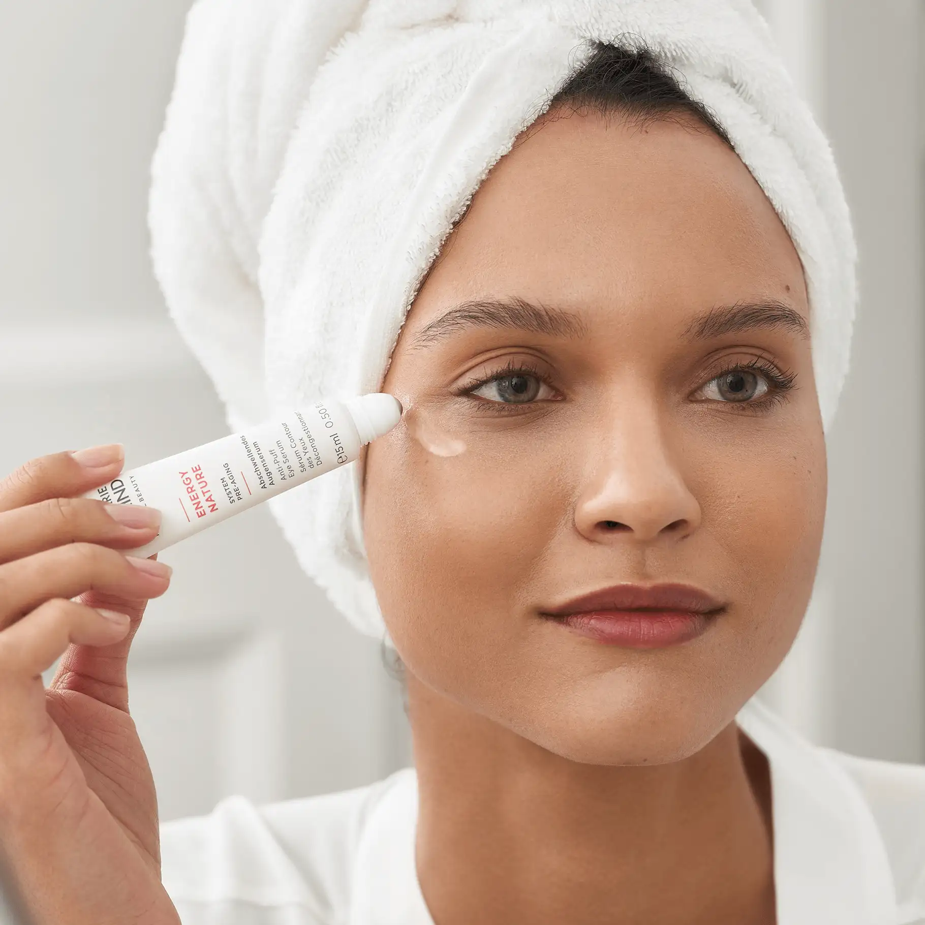 Frau mit Handtuch auf dem Kopf trägt ANNEMARIE BÖRLIND ENERGY NATURE abschwellendes Augenserum auf unteres Augenlid auf