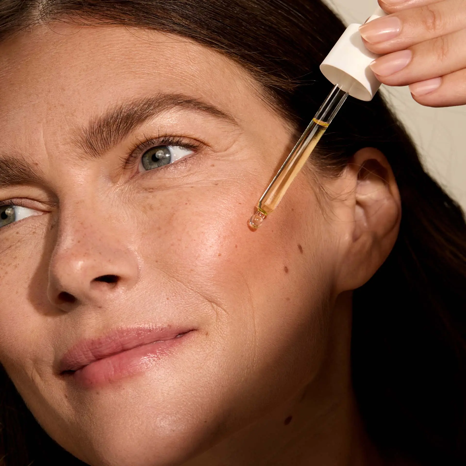 Frau hält Anti Aging Sun Protection Drops LSF 30 mit Pipette vor Gesicht