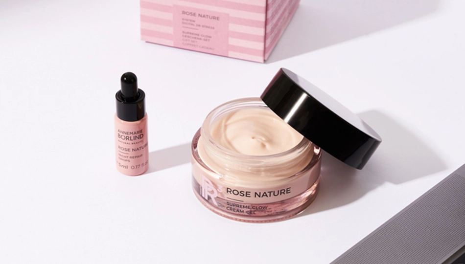 Hautalterung vorbeugen Pflegetipps Night Repair Drops und Supreme Glow Gel der ANNEMARIE BÖRLIND ROSE NATURE Pflegeserie auf einem Tisch. Der Tiegel des Gels ist geöffnet, im Hintergrund ist die Faltschachtel zu sehen.