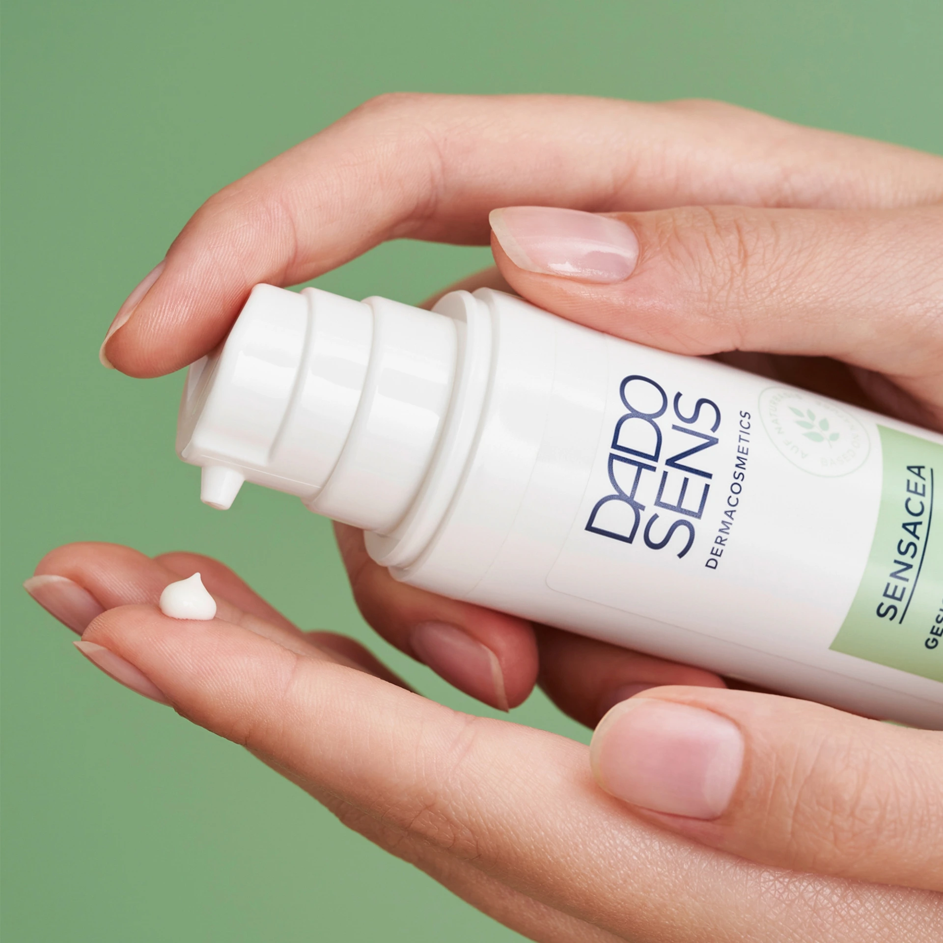 DADO SENS SENSACEA Gesichtsemulsion wird aus einem Spender auf die Fingerspitze dosiert vor grünem Hintergrund