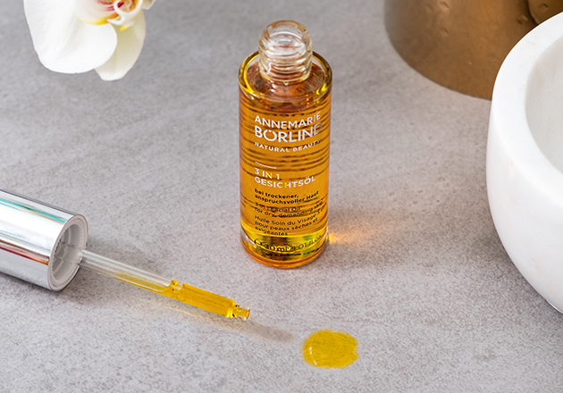 ANNEMARIE BÖRLIND 3 in 1 Gesichtsöl mit Pipette, goldgelbes Öl auf grauem Untergrund, Orchidee und Marmor zu sehen
