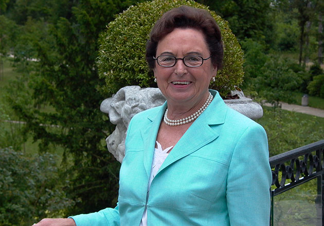 Annemarie Lindner lächelnd im Garten vor grüner Hecke und Steinfigur