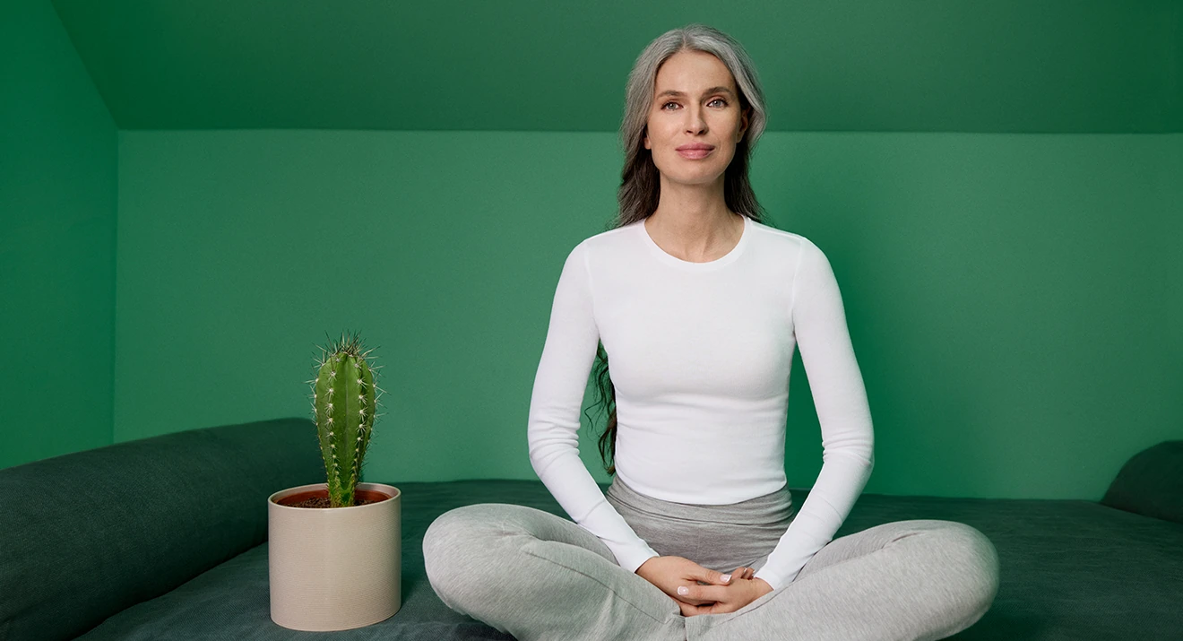 Frau sitzt entspannt neben einem Kaktus – Symbolbild für Trockenheit und Juckreiz im Intimbereich in den Wechseljahren