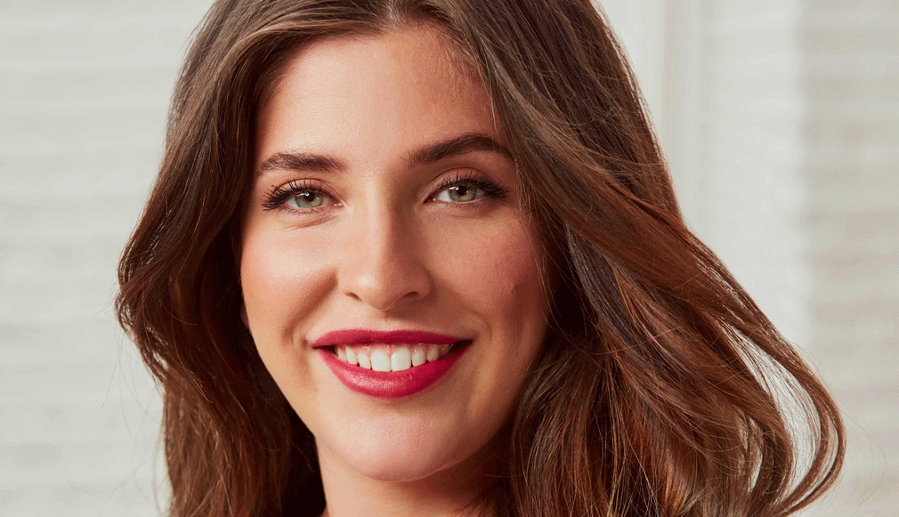 Nahaufnahme einer lächelnden Frau mit roten Lippen, dezentem Augen-Make-up und offenem braunem Haar