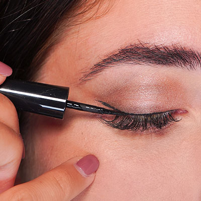 Nahaufnahme einer Hand, die flüssigen Eyeliner am oberen Wimpernkranz eines geschlossenen Auges aufträgt