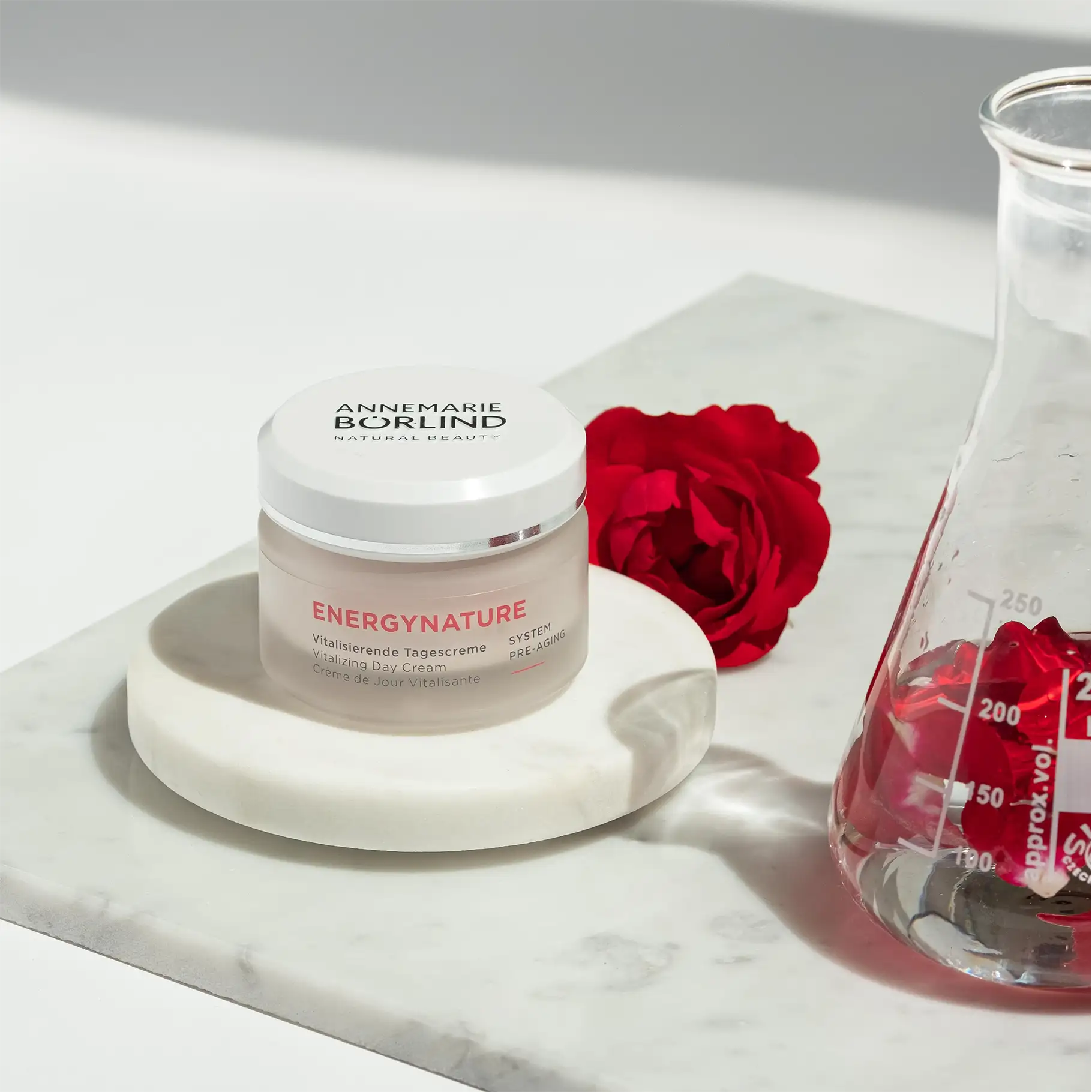 ANNEMARIE BÖRLIND ENERGYNATURE vitalisierende Tagescreme im Tiegel mit roten Rosen und Glasgefäß auf Marmorplatte