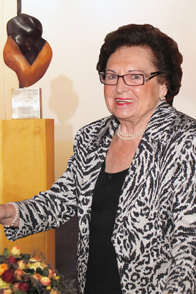 Annemarie Lindner mit Brille und Perlenkette neben einer abstrakten Skulptur auf Holzsockel in Innenraum