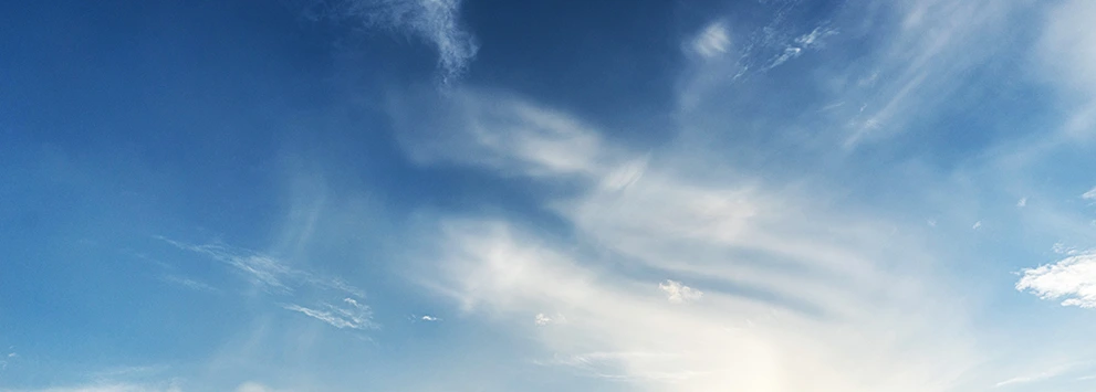 Blauer Himmel mit vereinzelten weißen Wolken und hellem Sonnenlicht am Horizont