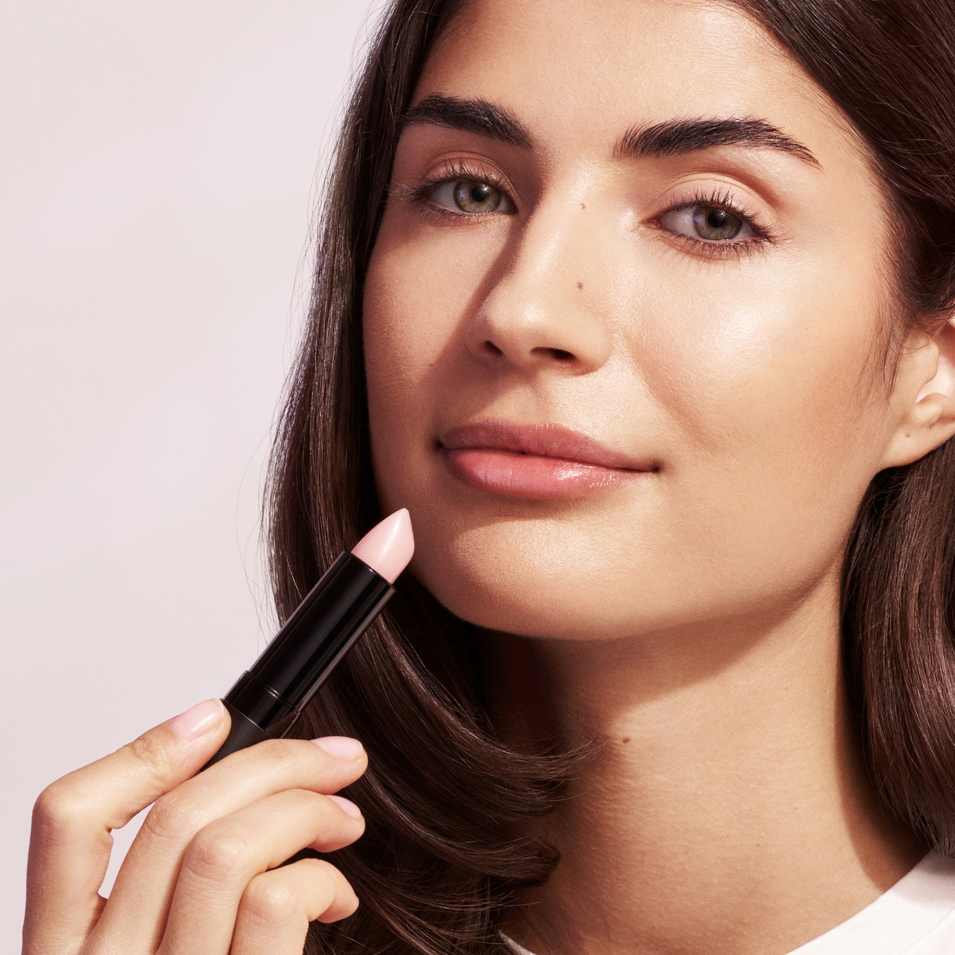 Frau hält ANNEMARIE BÖRLIND Natural Lip Glow Lippenstift in hellem Rosé nah an ihr Gesicht