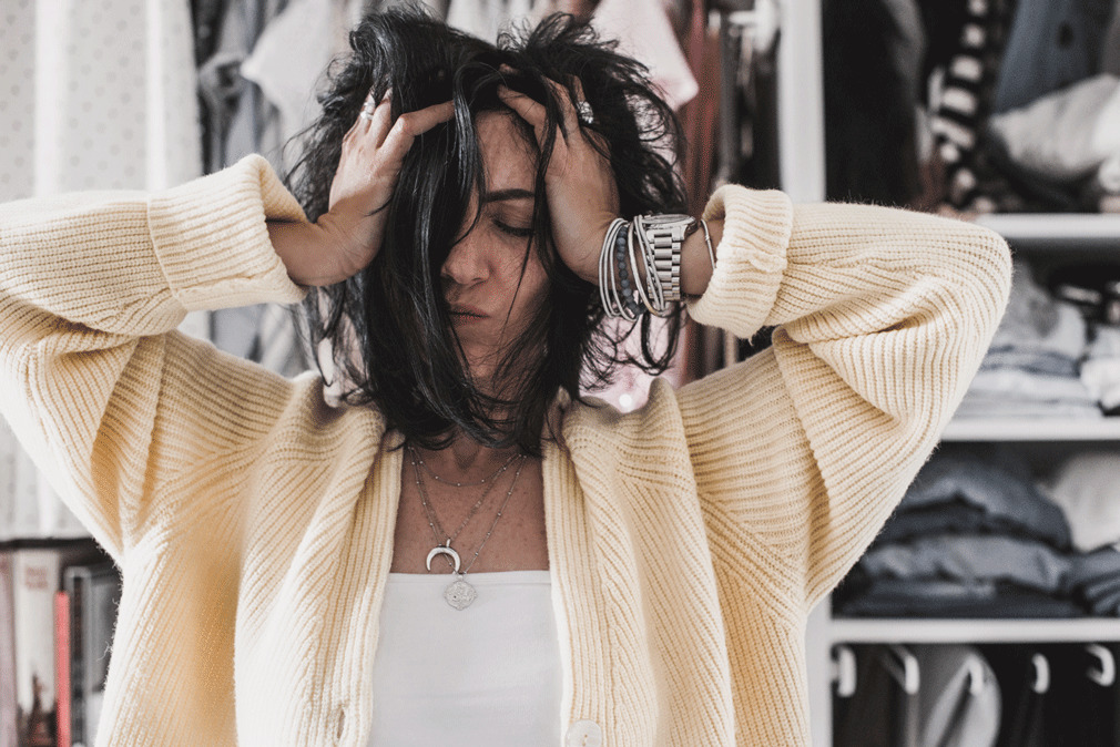 Frau hält sich mit geschlossenen Augen und verstrubbtem Haar den Kopf, wirkt gestresst oder erschöpft