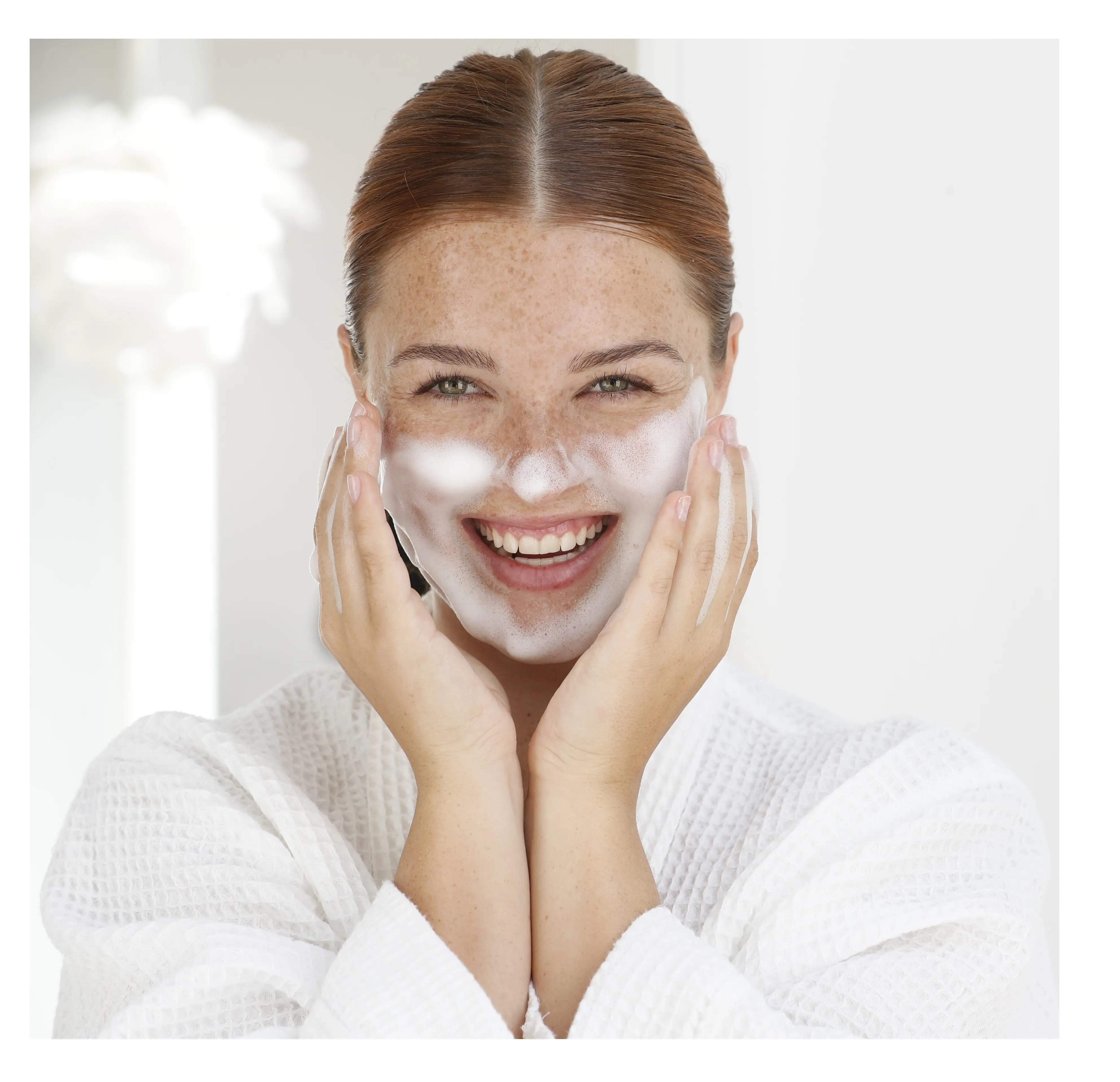 Frau wäscht Gesicht mit Schaum, trägt weißen Bademantel, lächelt in hellem Raum