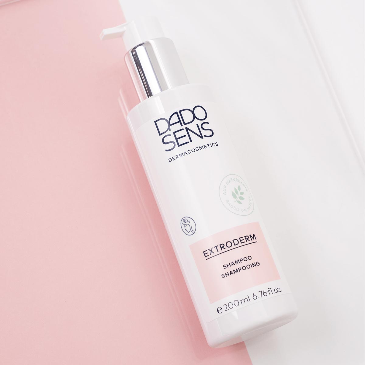 DADO SENS EXTRODERM Shampoo in weißer 200-ml-Flasche mit Pumpspender auf rosa-weißem Hintergrund