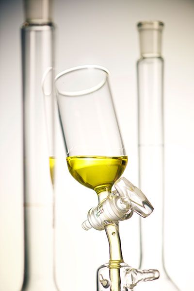 Glasapparatur mit gelblicher Flüssigkeit vor unscharfen Glaszylindern in hellem Licht