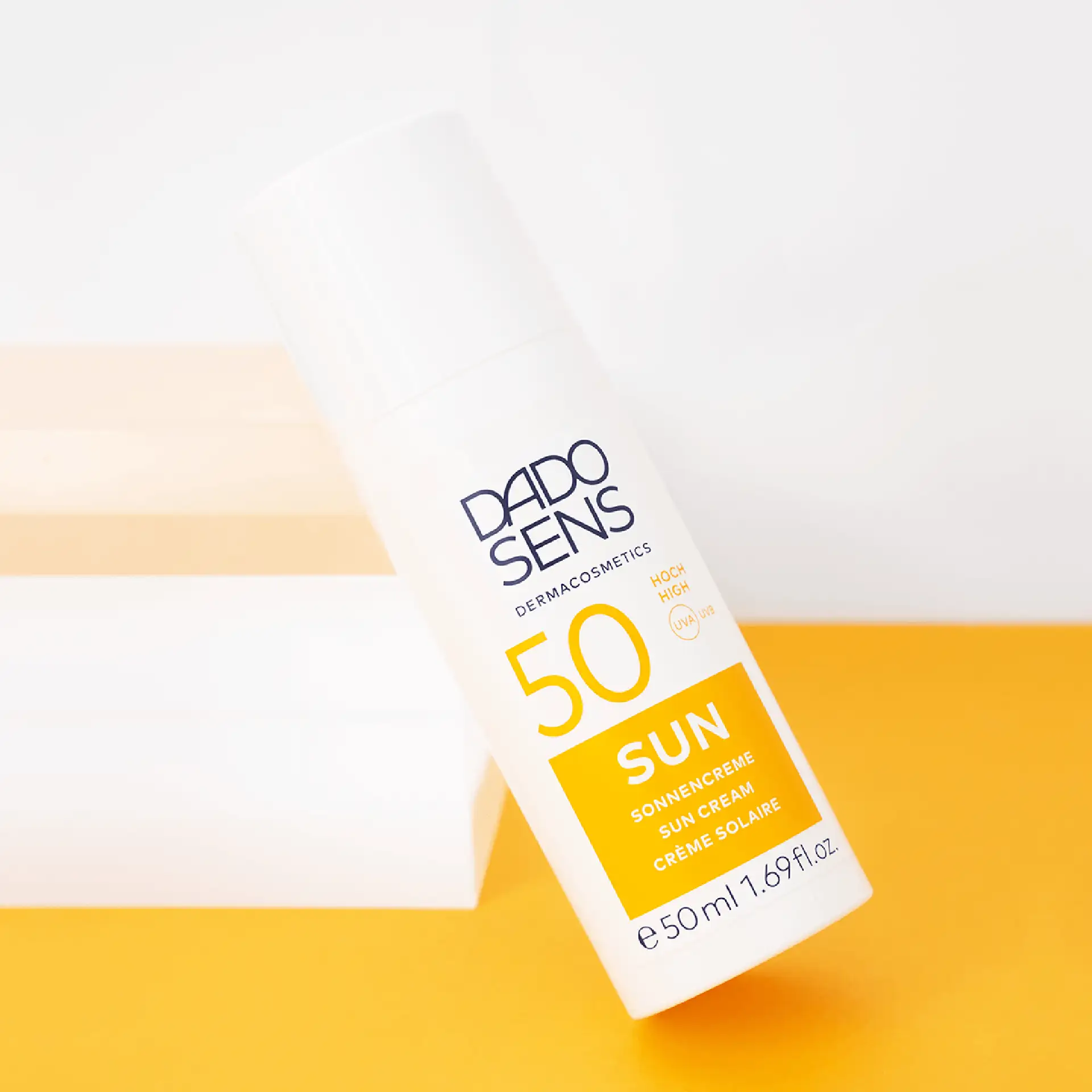 DADO SENS SUN Sonnencreme SPF 50 in 50 ml weißer Pumpflasche vor gelbem Hintergrund