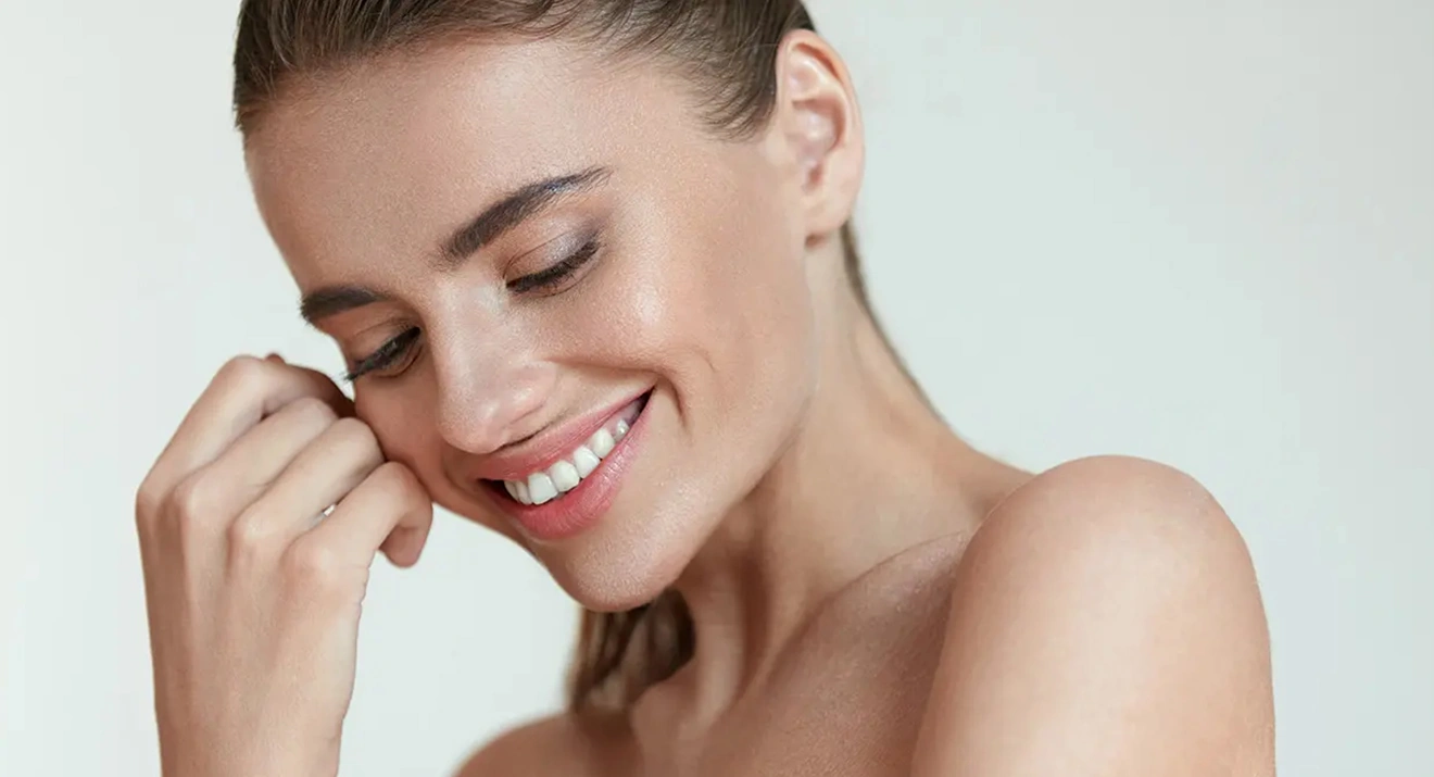 Nahaufnahme einer lächelnden Frau mit zurückgebundenem Haar und beruhigtem, ebenmäßigem Teint – dezentes Make-up für empfindliche Haut.