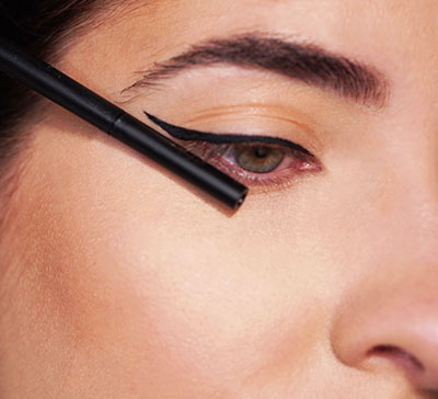 Nahaufnahme eines Auges mit präzisem schwarzem Lidstrich und einem Eyeliner-Stift am äußeren Augenwinkel