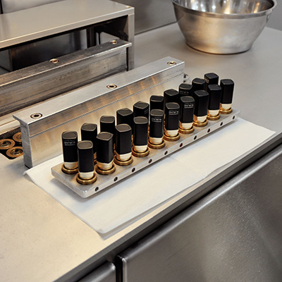 Reihe von Lippenstiften in schwarzem und goldenem Design in einer Metallform auf einer Edelstahl-Arbeitsfläche