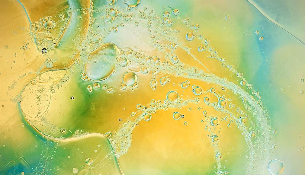 Nahaufnahme von transparenten Ölblasen in gelb-grün-blauem Flüssigkeitsgemisch mit Lichtreflexionen