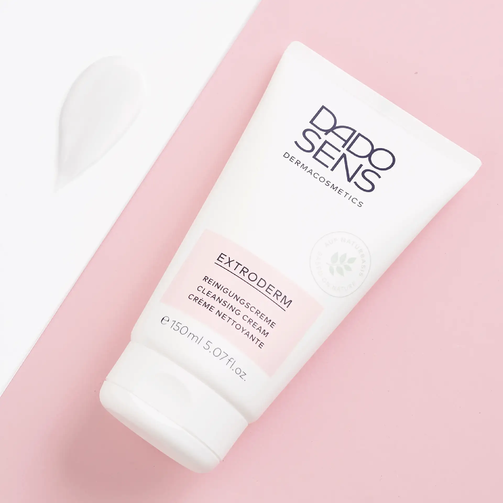 DADO SENS EXTRODERM Reinigungscreme 150 ml Tube mit cremiger weißer Textur auf rosa Hintergrund